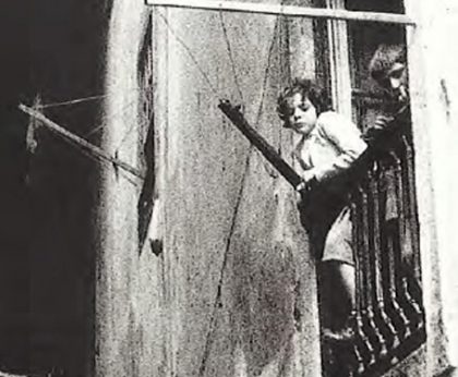 Fotografia a preto e branco com criança à Janela em Bairro Urbano nos anos 70